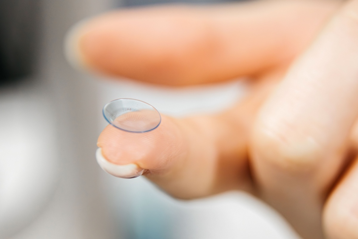 Person holding a contact lens on their fingertip.